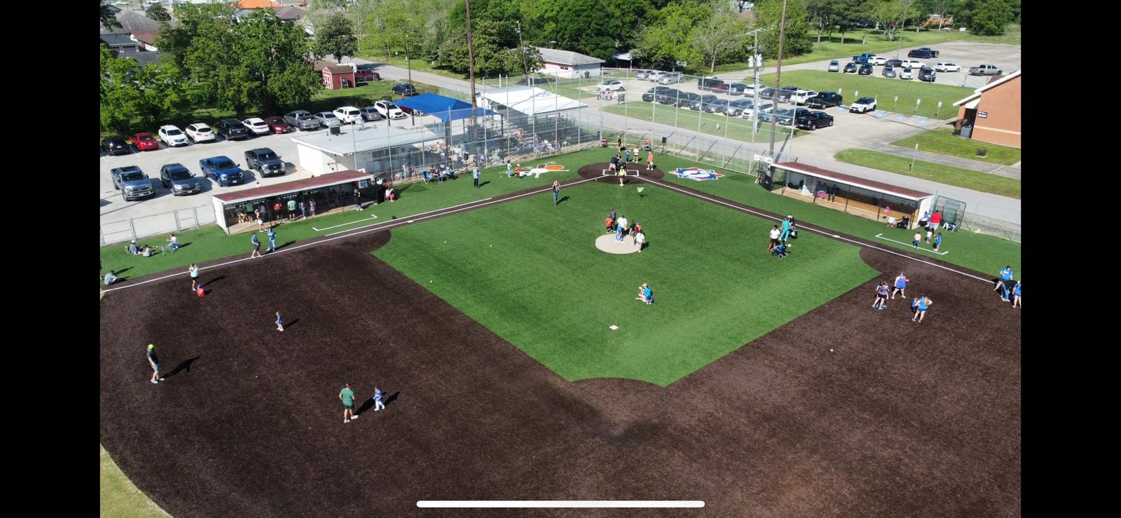 Aerial view of an artificial turf baseball diamond with people on the field