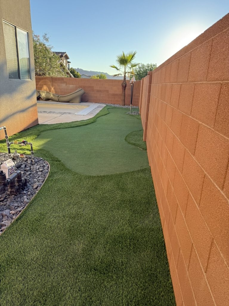 Artificial turf putting green and side yard running along a block wall beside a pool deck
