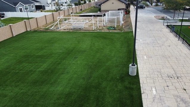 Artificial turf area beside stored soccer goals, next to a paver walkway with lamp posts
